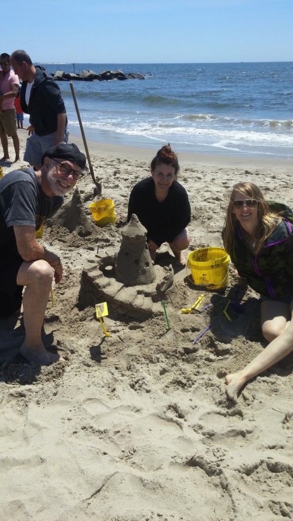 man and two women smiling around sand castle